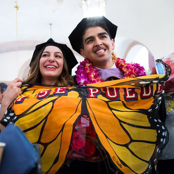 Two School of Dentistry graduates hold a "Si se Puede" banner.